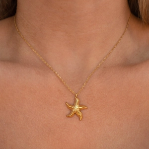 Macro shot of 18k gold starfish pendant with textured grain detail on cable chain