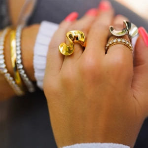 Detailed view of stacked 18k gold-plated S-shape rings and diamond tennis bracelets on wrist