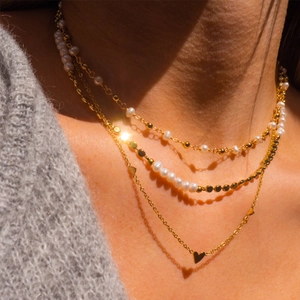 Collier doré à trois rangs avec perles blanches et pendentifs cœurs sur pull gris