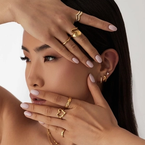 Detail shot of stacked 18K gold plated rings, earrings and chain on model skin