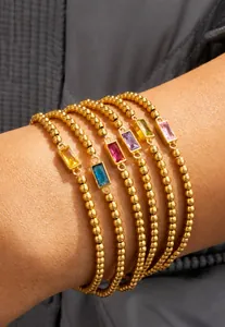 Set van zes gouden kralenarmbanden met kleurrijke rechthoekige edelstenen op een pols