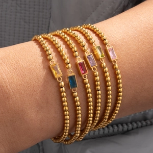 Detailweergave van gestapelde gouden kralenarmbanden met kleurrijke geboortestenen