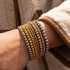 Detail von 18K gold- und silberplattierten Perlenarmbändern auf einem weichen Wollpullover