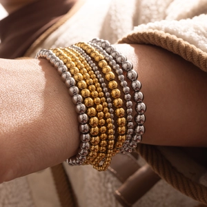 Nahaufnahme von gold- und silberfarbenen elastischen Perlenarmbändern am Handgelenk