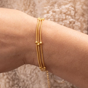 Detail eines 18K vergoldeten dreilagigen Schlangenarmbands mit polierten Perlen am Model