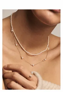 Detail einer mehrlagigen Gold-Perlenkette und eines Herzrings an einem Model