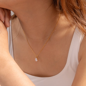 Primo piano di una collana a goccia in acciaio placcato oro 18k con zircone su una modella