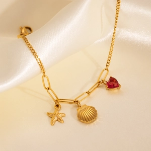 Detail of 18k gold chain with starfish, shell and red heart gemstone on silk background