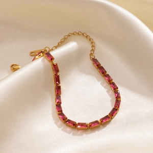 Detail view of gold-plated bracelet with rose red square zircons on beige satin silk