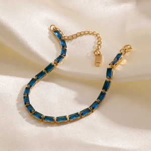 Detailed view of golden tennis bracelet with blue square zircon stones on silk fabric