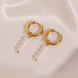 Detailed close-up of gold stainless steel pearl drop earrings on white silk fabric