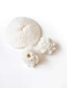 Close-up of white plush curly wool ball earrings with gold bead detail on coral background