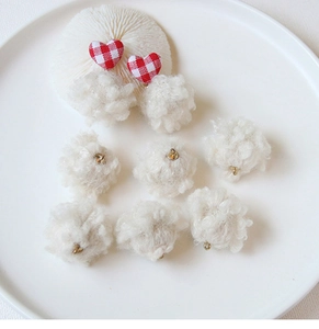 Close-up of DIY plush ball pendants with red heart accents on a white porcelain tray