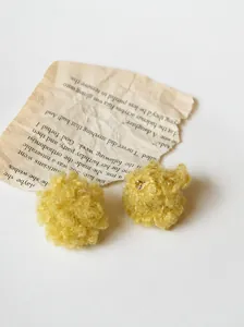 Dettaglio macro di orecchini a pompon gialli su sfondo di carta vintage