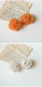 Dettaglio di orecchini a pompon arancioni e crema con perline dorate su carta vintage