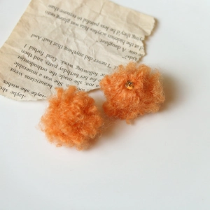 Orecchini a perno con pompon in mohair arancione su sfondo di carta d'epoca vintage