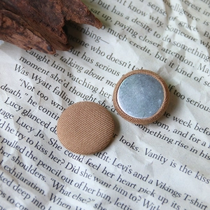 Close-up of round khaki fabric covered buttons with silver metal back on vintage paper