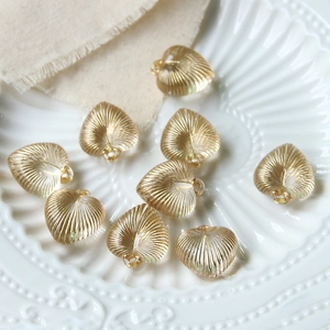 Golden heart-shaped ribbed glass beads for jewelry making displayed on a white plate