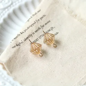 Macro shot of two golden diamond-shaped earrings on a rustic fabric background