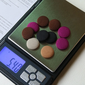 Set of round fabric covered buttons in various colors on a digital scale weighing 5.40g