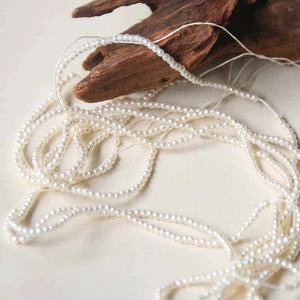 Perlas artificiales blancas redondas de 3mm esparcidas en mesa con decorado de madera
