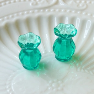 Detailed close-up of green miniature fluted glass vases with ruffled edges on white ceramic
