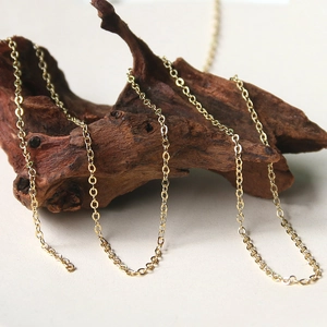 Detail of elegant gold-plated rollo chain draped on driftwood with polished finish
