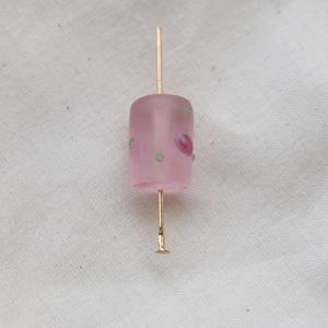 Macro shot of pink frosted glass cylinder bead with polka dots on a metal jewelry pin