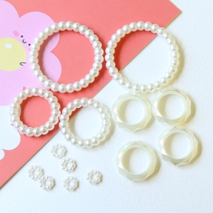 Flat lay of faux pearl bead rings and translucent geometric resin rings on soft background