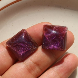 Detailed macro view of square resin charms with gold thread inclusions on fingers
