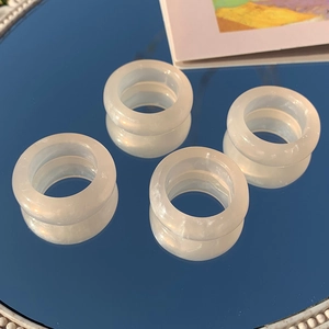 Close-up of four translucent milky white resin rings with pearlescent finish on blue mirror