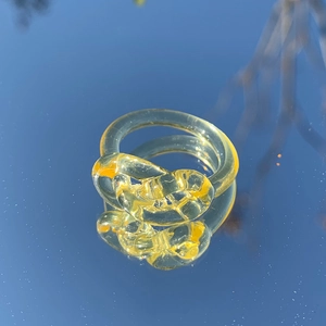 Nahaufnahme eines gelben transparenten Harzknotenrings, der den blauen Himmel spiegelt