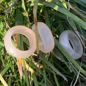 Macro view of three minimalist cream white and pink resin rings on a natural green background