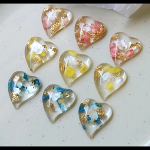 Macro shot of heart-shaped resin charms with dried flowers and gold foil accents