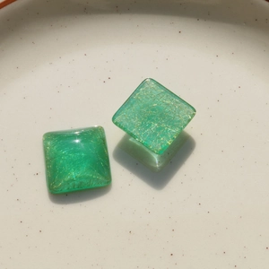 Macro detail of square green resin charms with gold thread texture for DIY jewelry