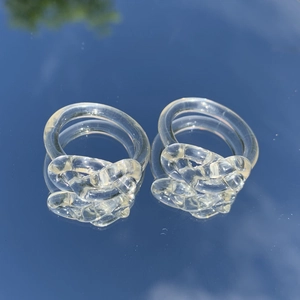 Makroaufnahme von zwei transparenten Harzringen mit Twist-Design auf einer Spiegelfläche