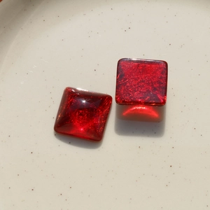 Macro shot of square translucent red resin charms with golden glitter fibers for DIY jewelry