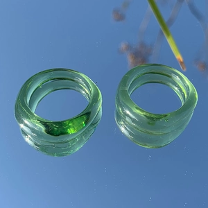Macro di due anelli irregolari in resina verde smeraldo rifletti su una superficie specchiata
