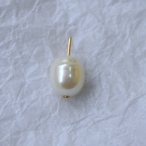 Dettaglio di una perla d'acqua dolce bianco crema con perno dorato su carta ruvida
