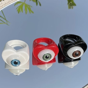 Macro detail of Y2K heart rings with resin eyes reflecting a blue sky on a mirror surface
