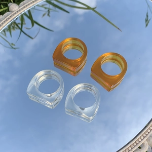 Primer plano de anillos geométricos de resina transparente y ámbar sobre espejo