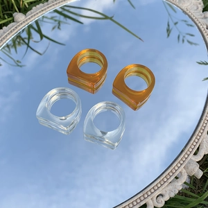 Anillos minimalistas de resina transparente y ámbar sobre espejo que refleja el cielo