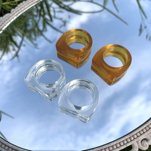 Primer plano de anillos minimalistas de resina transparente y ámbar reflejando el cielo