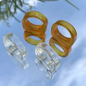 Anillos minimalistas de resina transparente en ámbar y claro sobre fondo de cielo reflejado