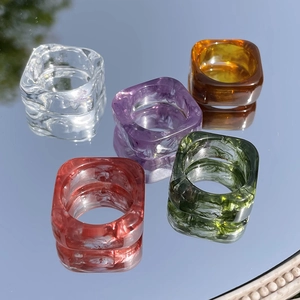 Close-up of square resin rings in amber and marble green colors on a reflective mirror