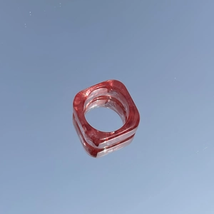 Macro view of square red resin ring with marbled ink texture on blue mirror