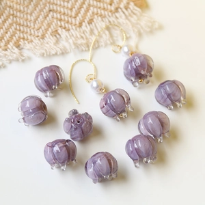 Detalle de cuentas de vidrio lila con aretes de perlas doradas sobre fondo suave decorado