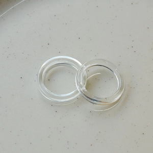 Macro shot of two minimalist transparent resin rings on a beige ceramic plate