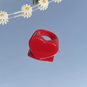 Glossy red heart-shaped resin ring displayed on a mirror reflecting clear blue sky