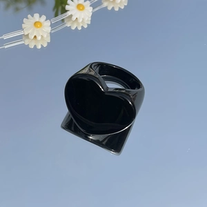 Minimalist glossy black heart ring reflecting clear blue sky with white daisies